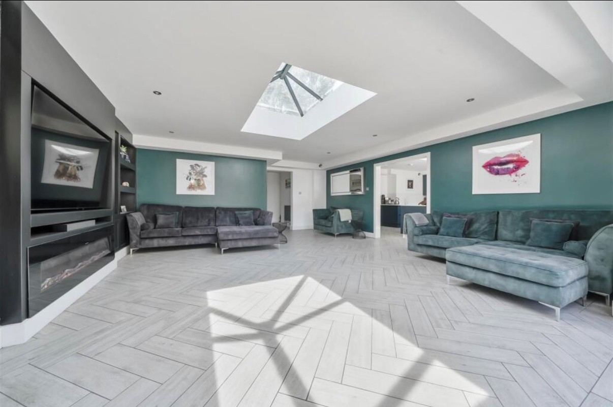 Open-plan living room with a roof lantern, two large corner sofas and a media wall